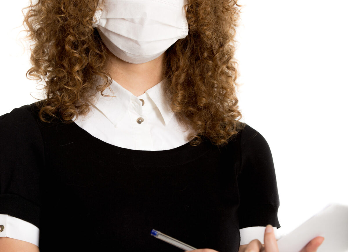 Girl wearing face mask and office uniform is writing   documents looks in camera